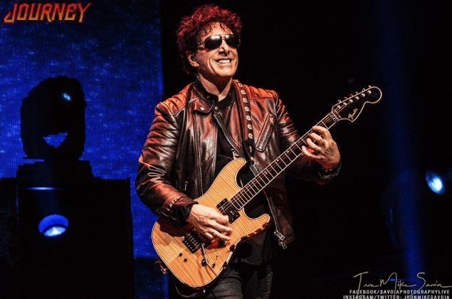 Neal schon plays guitar with a dark blue backdrop
